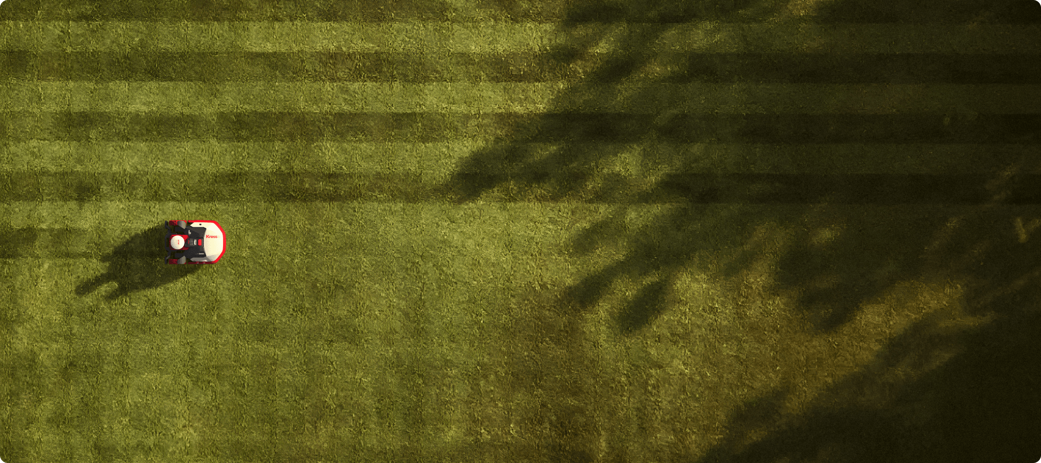 Aerial view of a Kress robotic mower cutting a grass on the field with shadows on the ground.