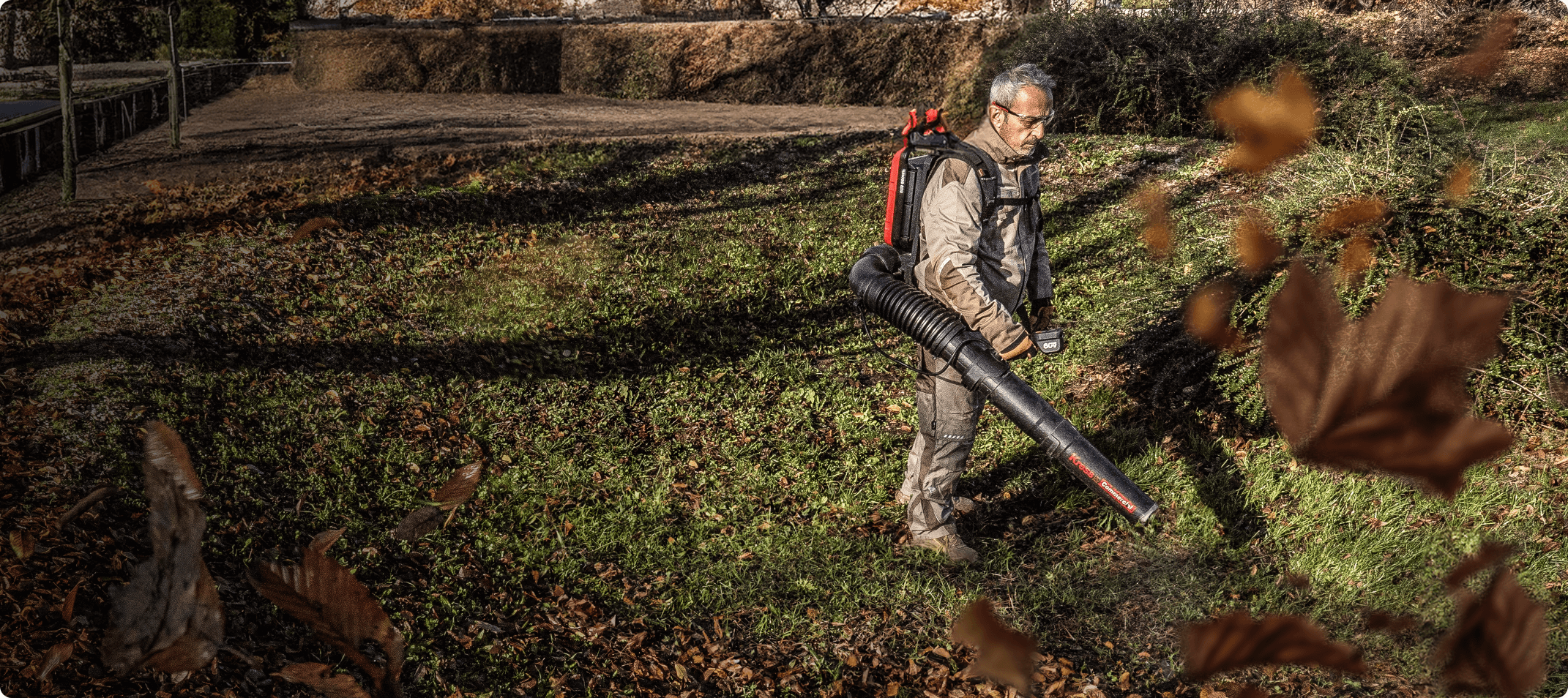 A man is using Kress backpack blower to blow the fallen leaves from the grass